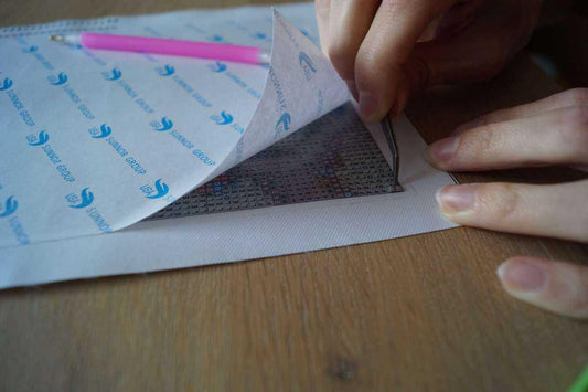 Een hand tilt de beschermfolie van een diamond-paintingcanvas