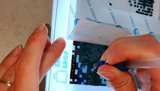 Hand plaatst steentjes op een klein werkvak terwijl de rest van het canvas afgedekt blijft